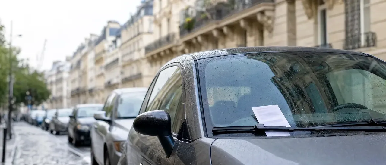 Avis de contravention glissé sous l'essuie-glace d'une voiture garée dans une rue de Paris